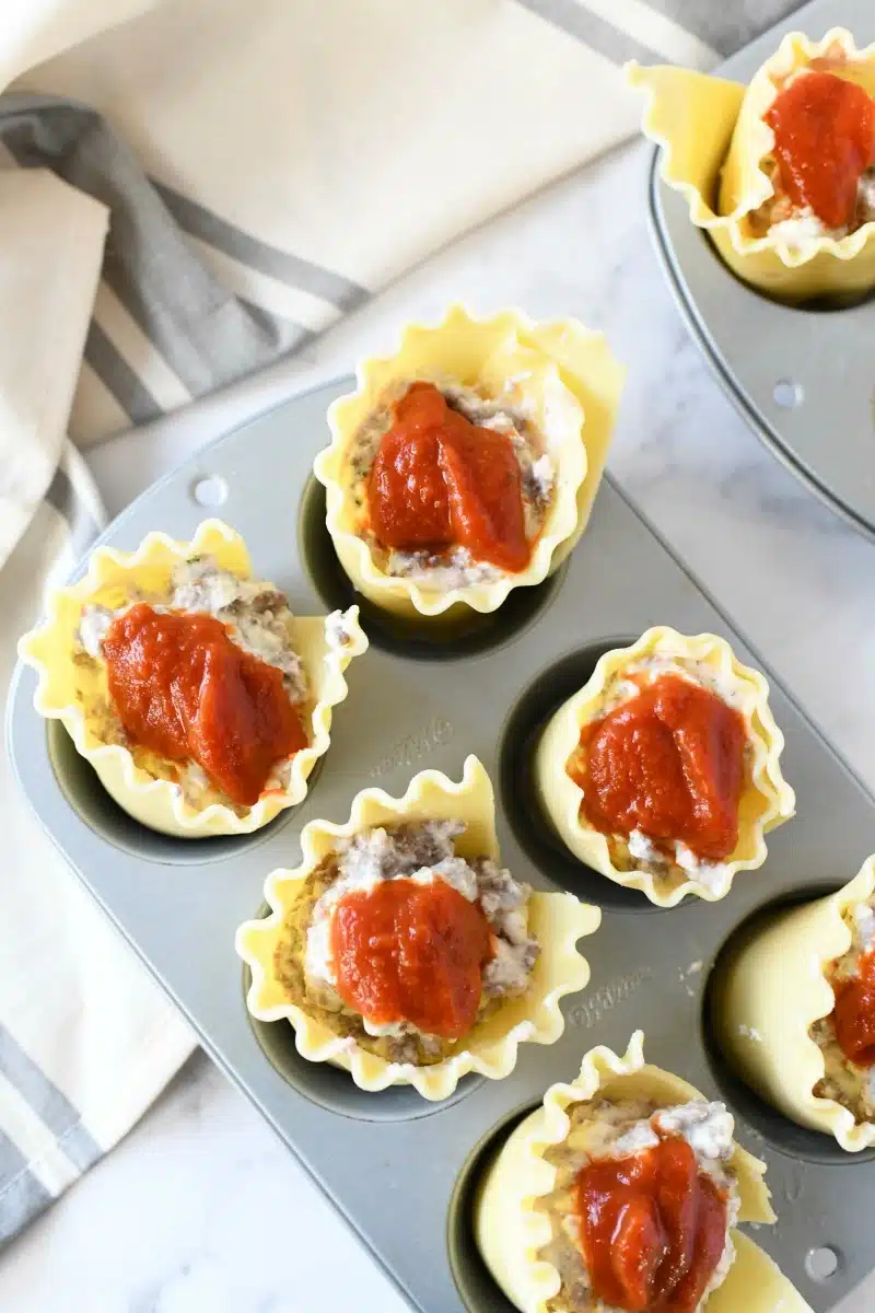 Lasagna roll ups with red sauce on them. They are placed in a muffin tin. 