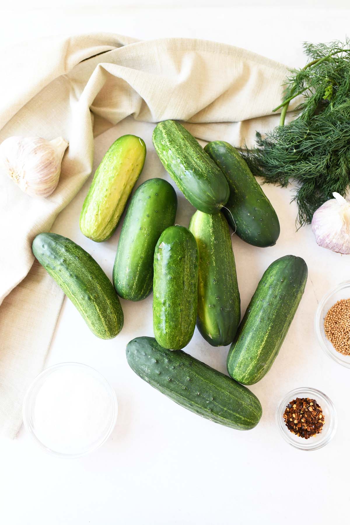Pickling cucumbers and spices on a white table with a napkin.