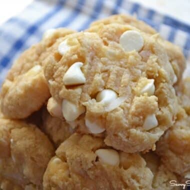 Baked, vanilla cookies with white chocolate chips on a blue, plaid napkin.