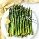 Oven roasted asparagus baked with lemon on a white plate with tongs.