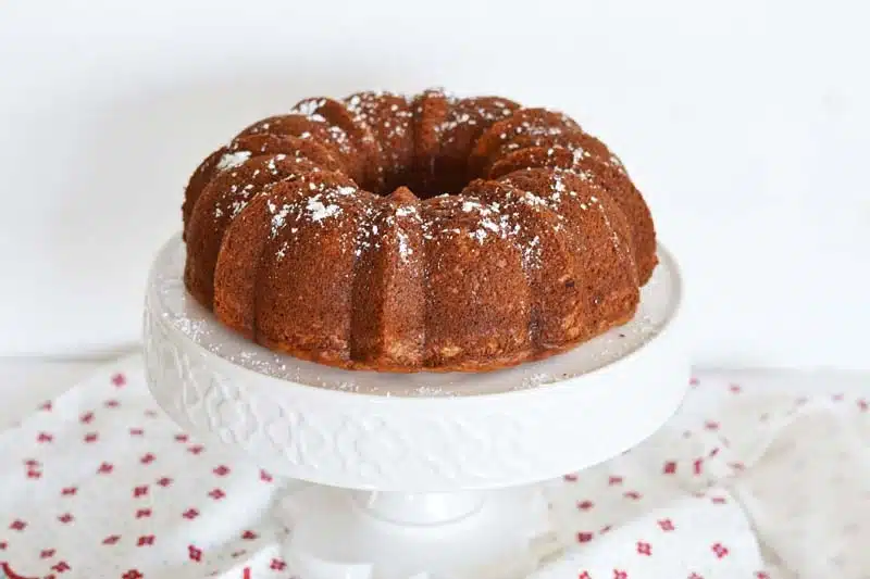 Banana Bundt Cake with Cream Cheese on a white cake stand. There is also a napkin on the table.