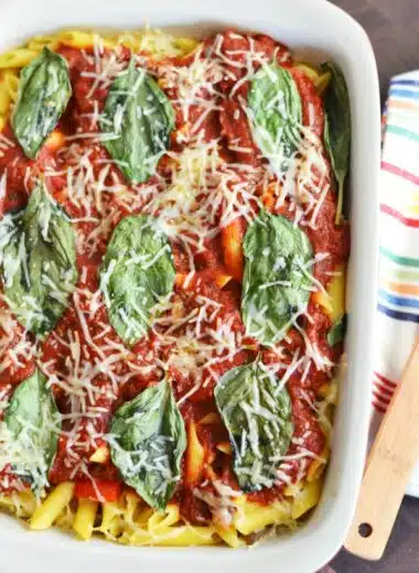 Mushroom pasta with parmesan cheese, and fresh basil in a white, rectangle baker.