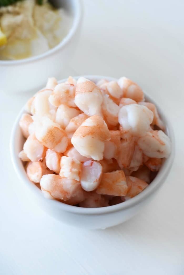 Cooked small shrimp in white bowl on white table.