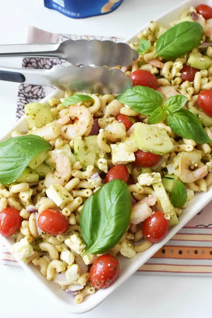 Shrimp Pesto Pasta Salad in serving tray with silver tong.