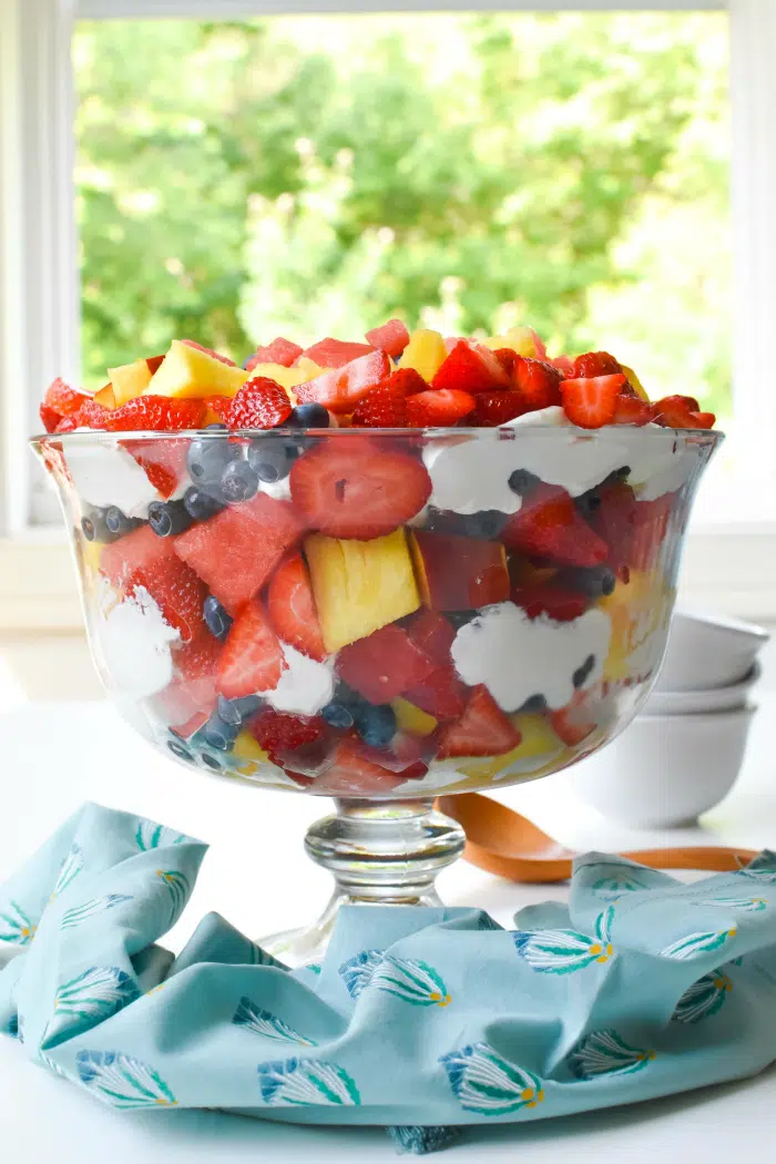 Side view of fruit Salad Trifle inside a glass bowl on table with blue napkin.