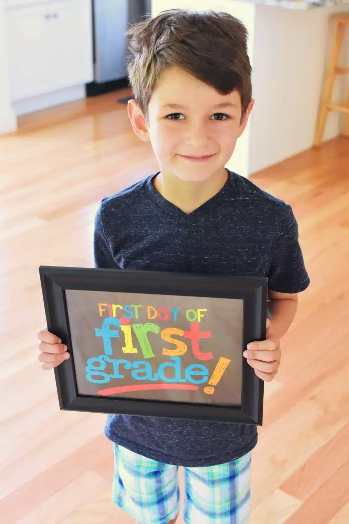 Boy holding first grade sign in a kitchen. 