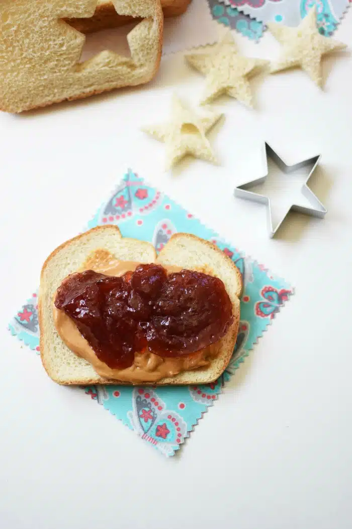 Peanut Butter and Jelly on sliced bread with a star cutout on the white table. 
