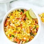Colorful corn salad in a white bowl with lime wedges.