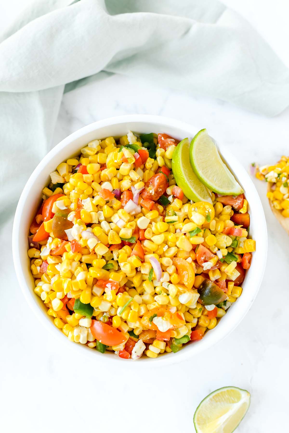 Colorful corn salad in a white bowl with lime wedges.