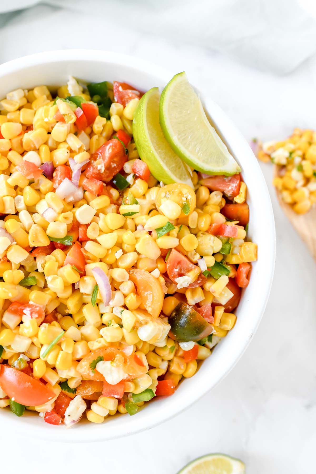 Zesty Corn salad in a white bowl with green lime wedges.