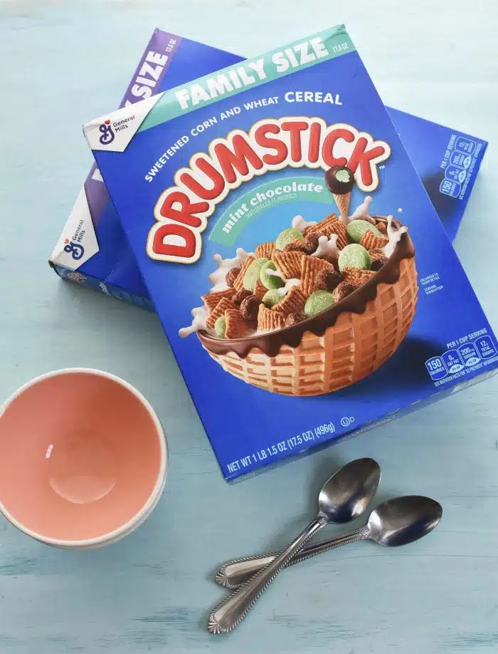 Family Size Drumstick Cereal boxes on blue table with bowls