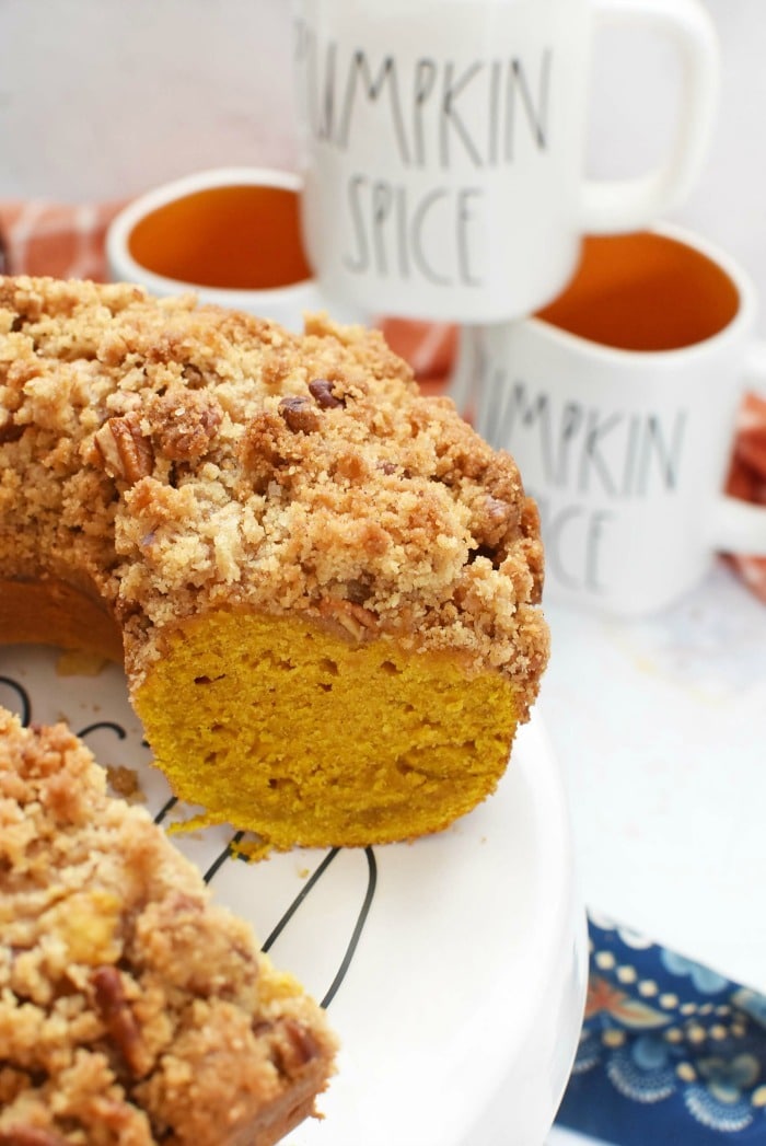 Pumpkin Streusel Bundt Cake on cake stand with Halloween mugs in background. 