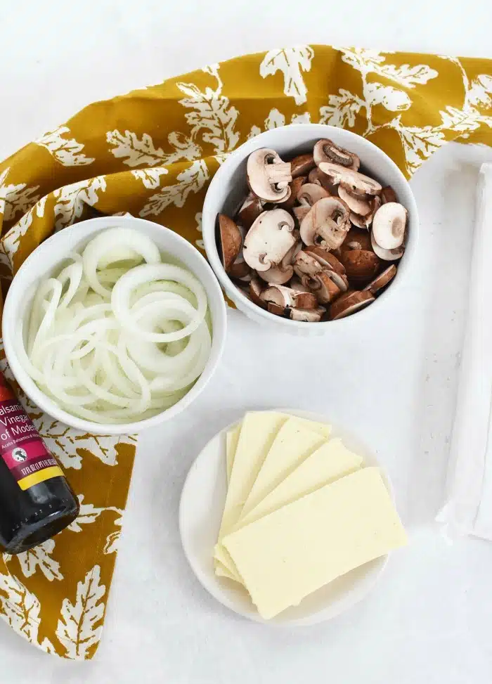 Balsamic Onions and Mushrooms with Cheese ingredients with gold colored napkin on a white table. 
