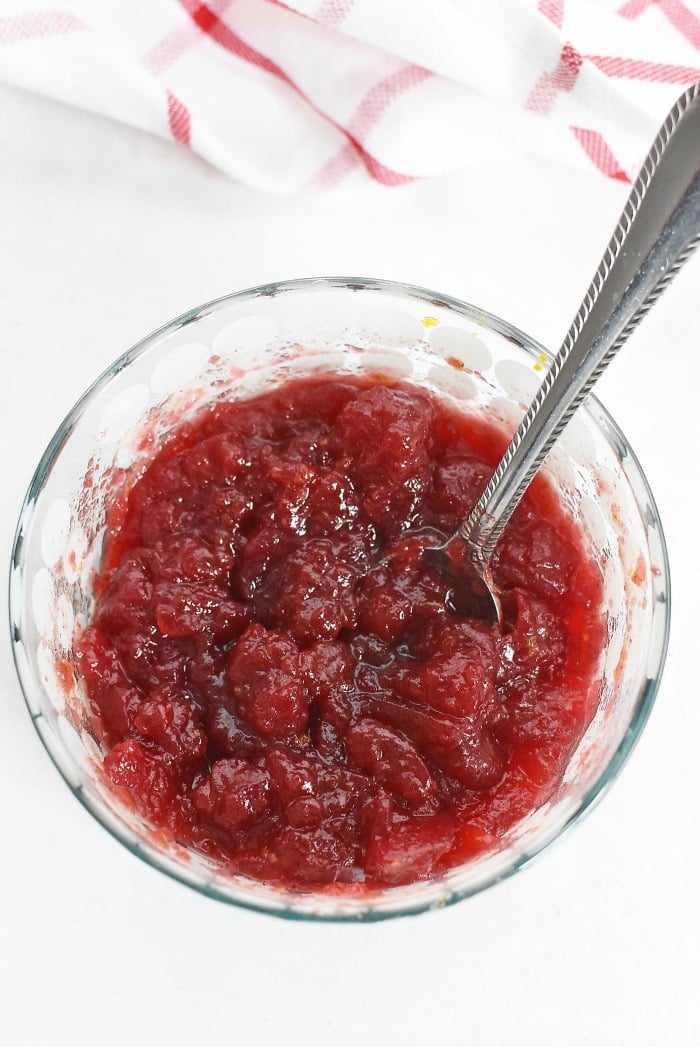 Crushed up cranberry sauce in a glass dish with a silver spoon. 
