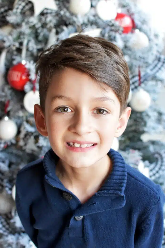 Boy smiling in front of Christmas tree. 