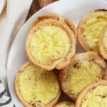 Custard Tarts in a white plate with a tan napkin, on a wood table.