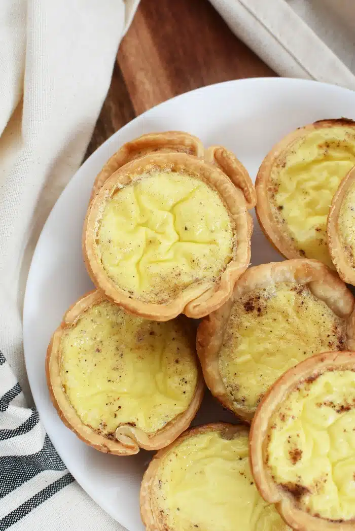 Custard Tarts in a white plate with a tan napkin, on a wood table. 