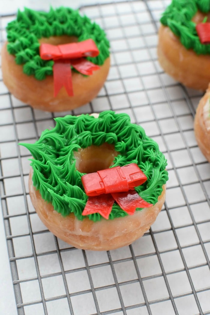 Donuts wreaths with red candy bow on baking sheet.