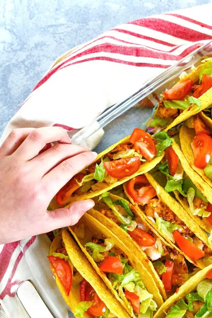Easy Chicken Taco Bake in glass dish with red striped towel. A hand is reaching in to grab a taco. 