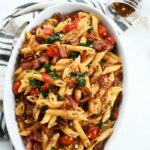 BLT Pasta in white oval dish with a striped towel and shaker of breadcrumbs.