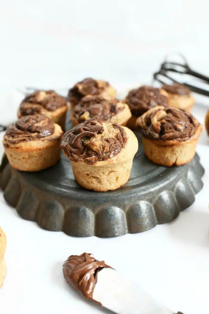 Nutella banana muffins on upside down pie dish tin with a Nutella lined knife. 