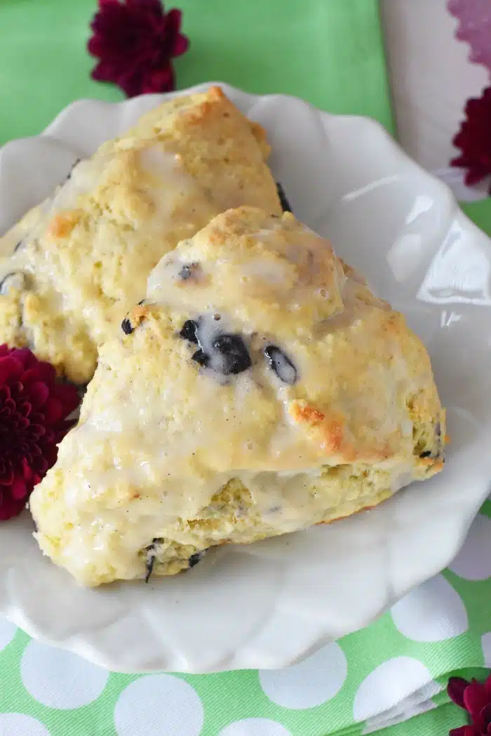 Blueberry scones on a white flowered plate with a green napkin and purple flowers. 
