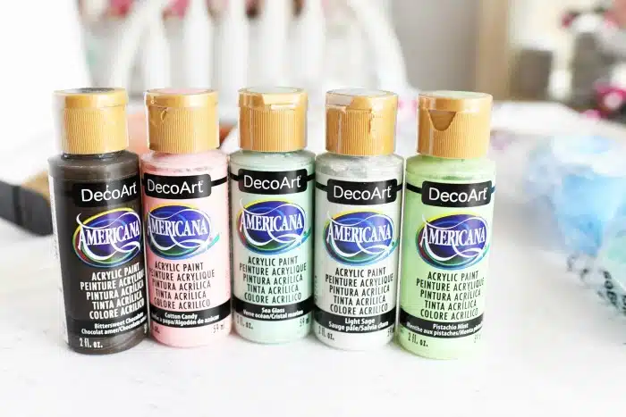 DecoArt Americana Paints lined up on white table. 