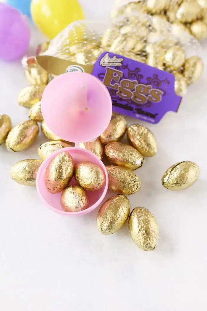 Gold foil eggs in pink plastic egg on white table. 