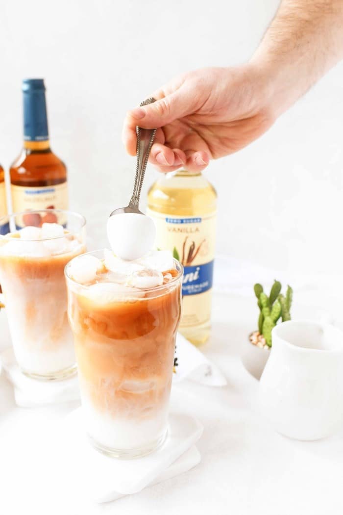 Hand pouring in almond milk foam over an iced tea latte. 