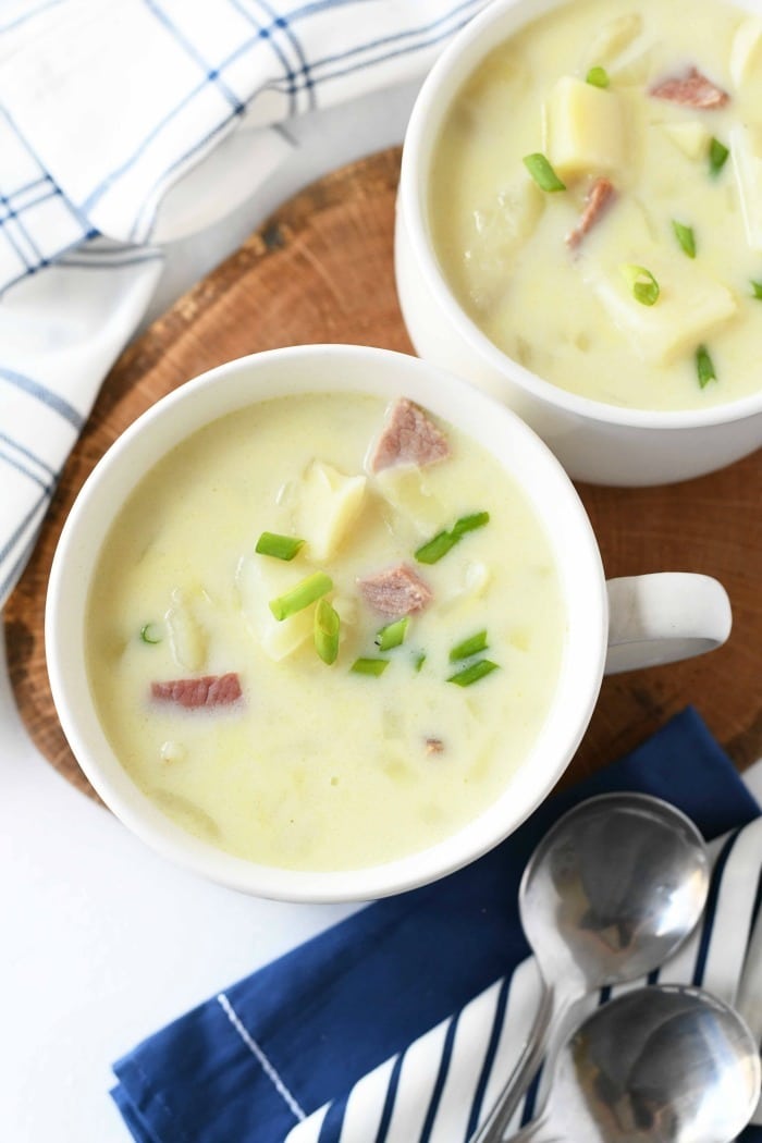 Spiral Ham Potato Soup in white crocks with spoons and a blue napkins. 