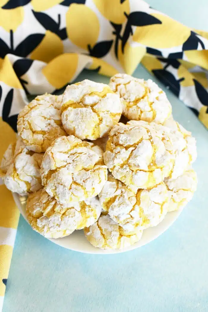 Lemon crinkle cake cookies on a white plate on a blue surface. 