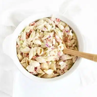 Crabmeat pasta salad in white dish with a wooden spoon.
