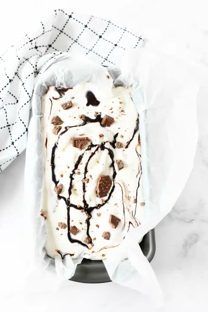 Home Chocolate Vanilla Swirl Crunch Ice Cream in loaf pan on white table.