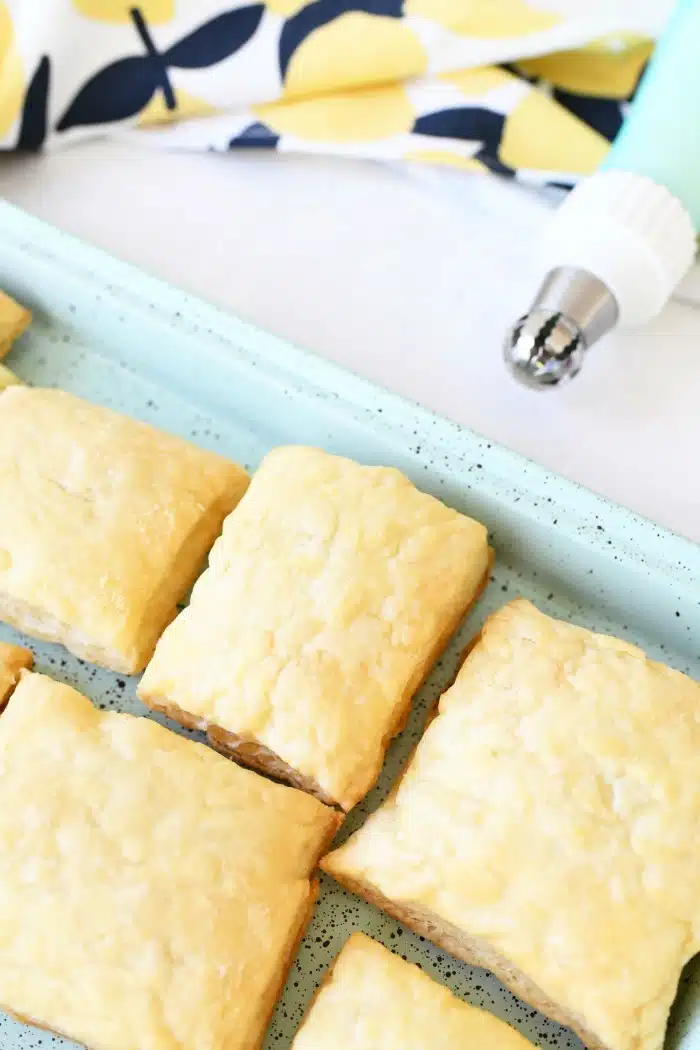 Puff pastry squares in a blue pan with piping bag nearby. 