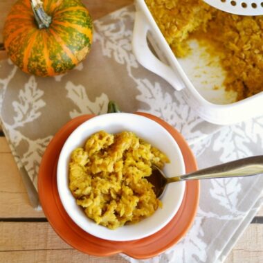 Baked Pumpkin oatmeal in a small white bowl with a spoon on a wooden table.