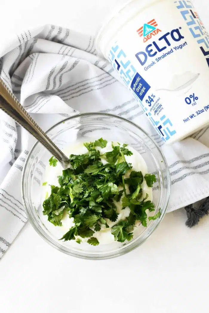 A glass bowl filled with Greek Yogurt and topped with cilantro. 