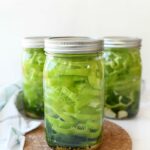 Cold packed Pickled Peppers in jars with lids on white table.
