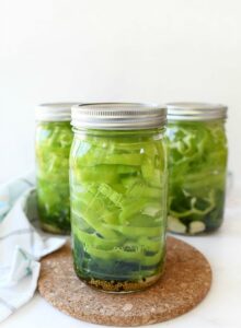Cold packed Pickled Peppers in jars with lids on white table.