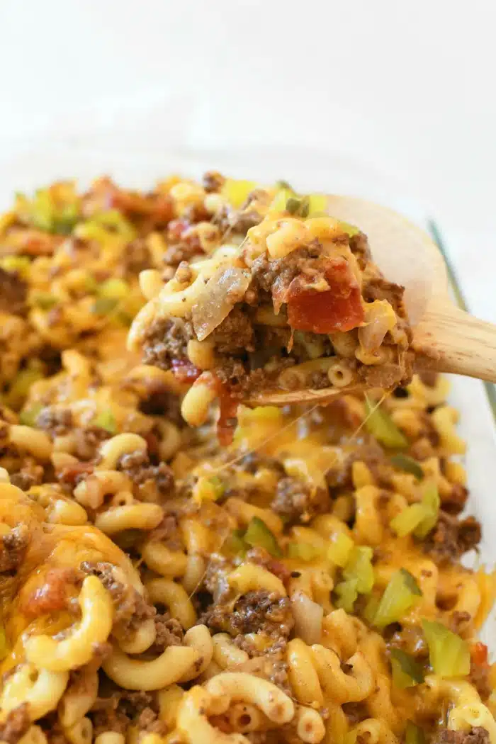Wooden spoon scooping Cheeseburger Casserole from white dish.