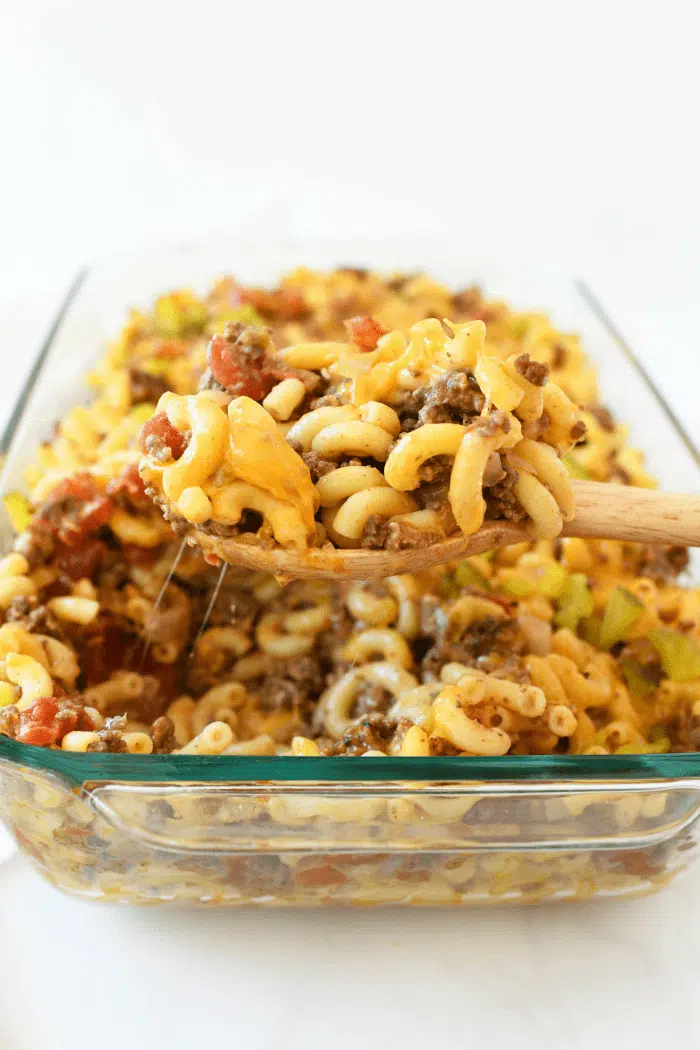 Cheeseburger pasta casserole scooped from glass pan with a wooden spoon.