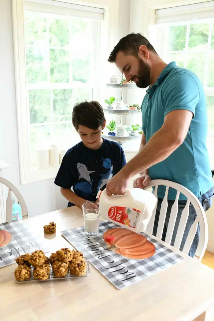 Dad pouring milk with son nearby.