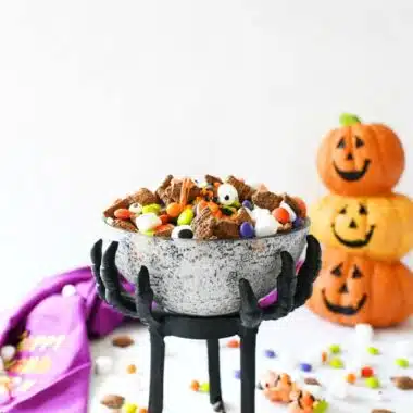 Halloween Muddy Buddys on a white table with pumpkins and candy.