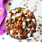 Halloween party mix in a dish with a purple towel on a white candy covered table.