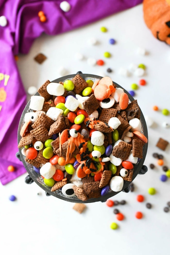 Halloween party mix in a dish with a purple towel on a white candy covered table.
