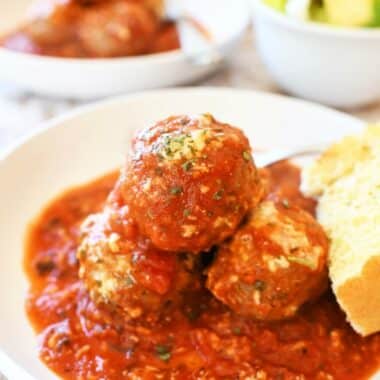 Cheesy meatballs casserole in a white dish with cheese and bread.