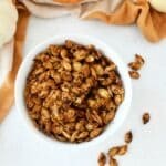 Spicy Baked Pumpkin seeds in a white bowl with an orange napkin and mini pumpkins.