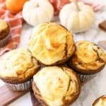 Cheesecake muffins on a wooden cutting board with mini pumpkins and an orange napkin nearby.
