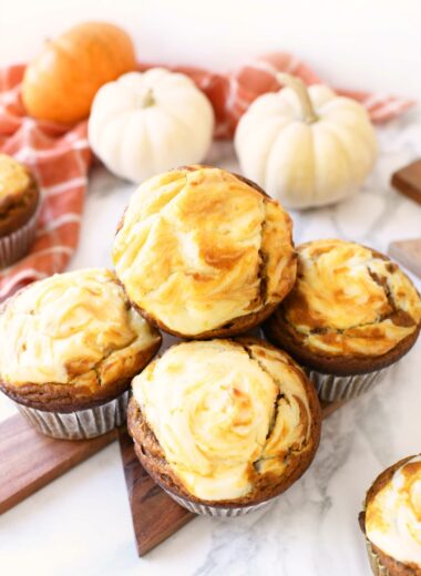 Cheesecake muffins on a wooden cutting board with mini pumpkins and an orange napkin nearby.