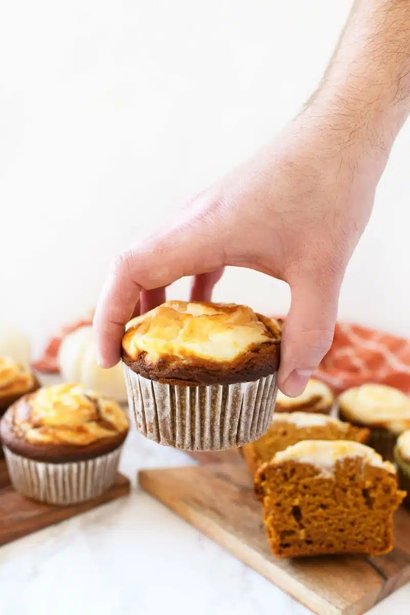 Man putting a pumpkin cream cheese muffin on a table near other muffins.