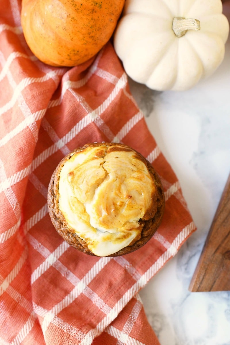 Pumpkin cheesecake muffins on an orange plaid napkin with mini pumpkins nearby.